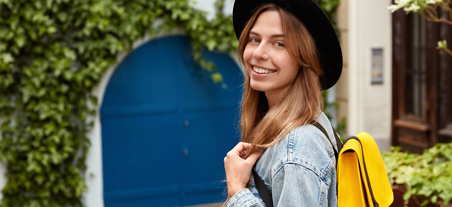 sideways-shot-cheerful-lovely-female-strolls-across-old-street-with-green-vegetation-wears